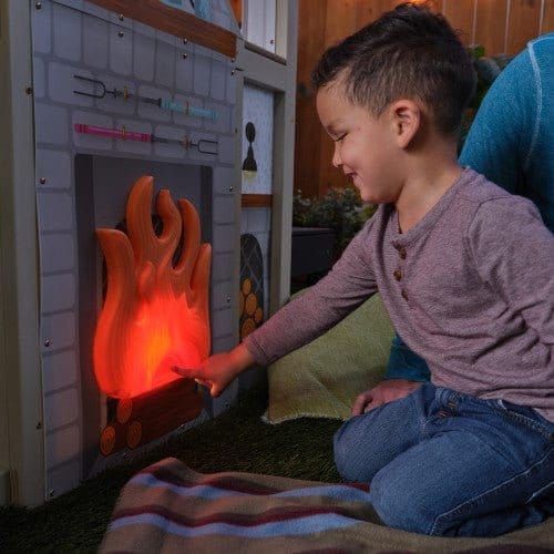 little boy kneeling by light up fire of KidKraft Cozy Hearth Cabin Playhouse