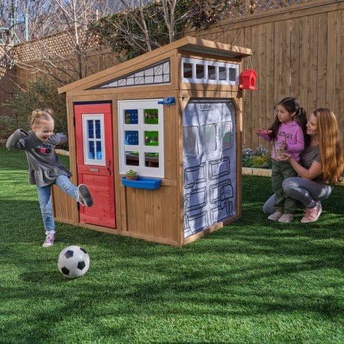 girl playing football in front of KidKraft Hobby Workshop Wooden Playhouse 