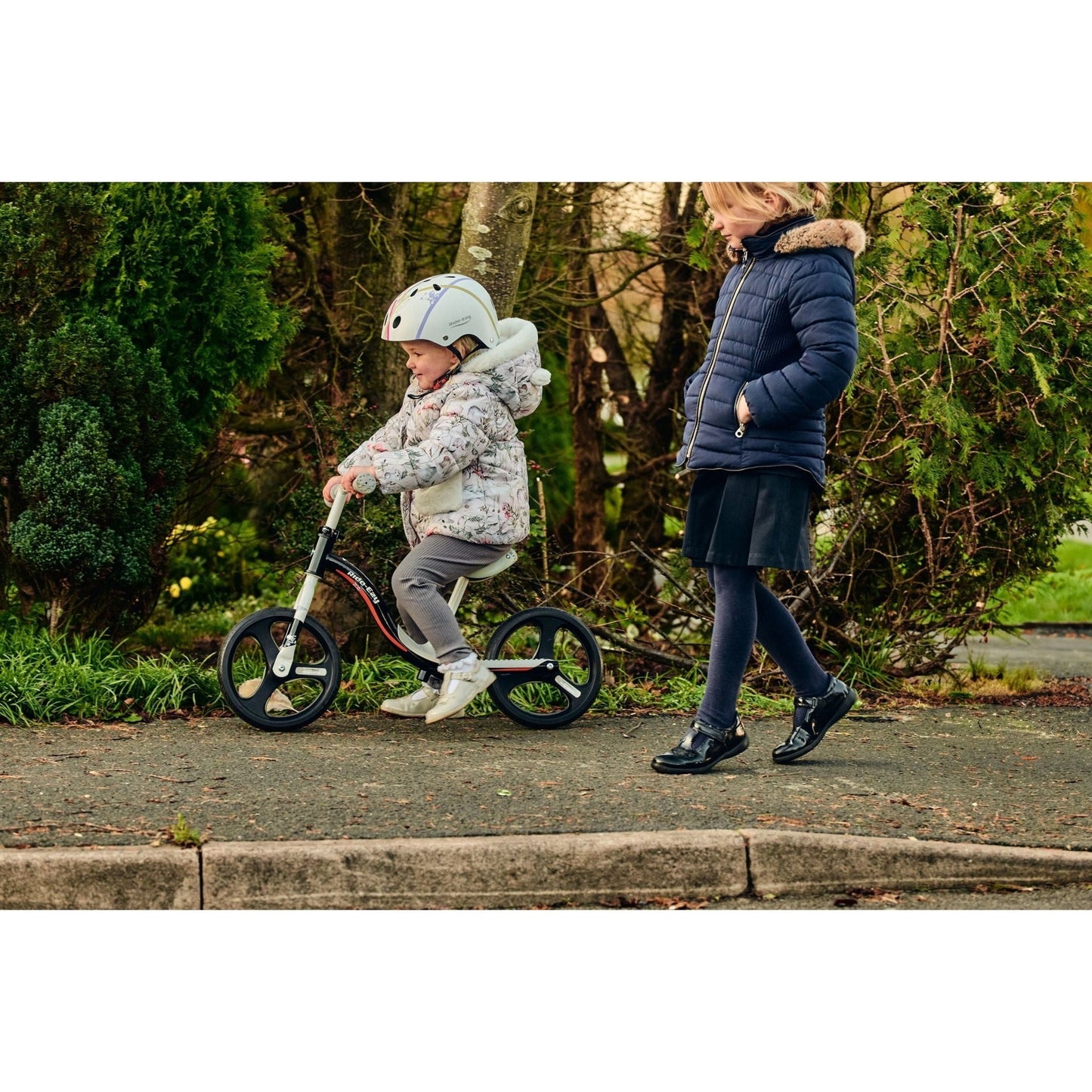 girl riding Ride-Ezy Go Glo Balance Bike - Black & Silver next to girl walking 