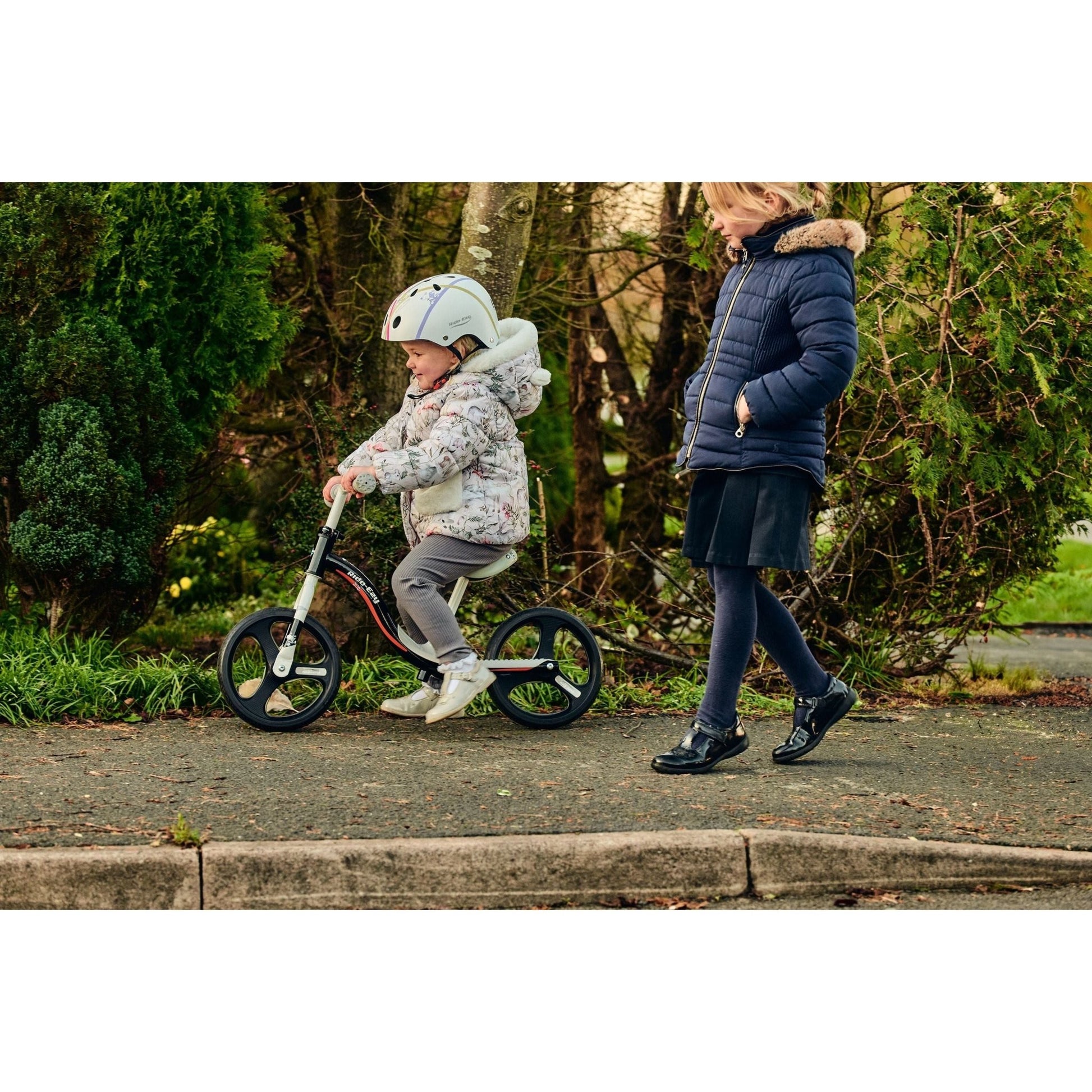 girl riding Ride-Ezy Go Glo Balance Bike - Black & Silver next to girl walking 