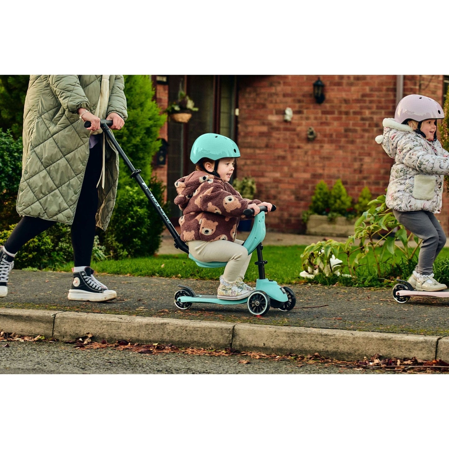 girl sitting on ride ezy kick scooter while wearing Ride-Ezy Hector 48-53cms Kids Helmet - Kingfisher and being pushed by mother