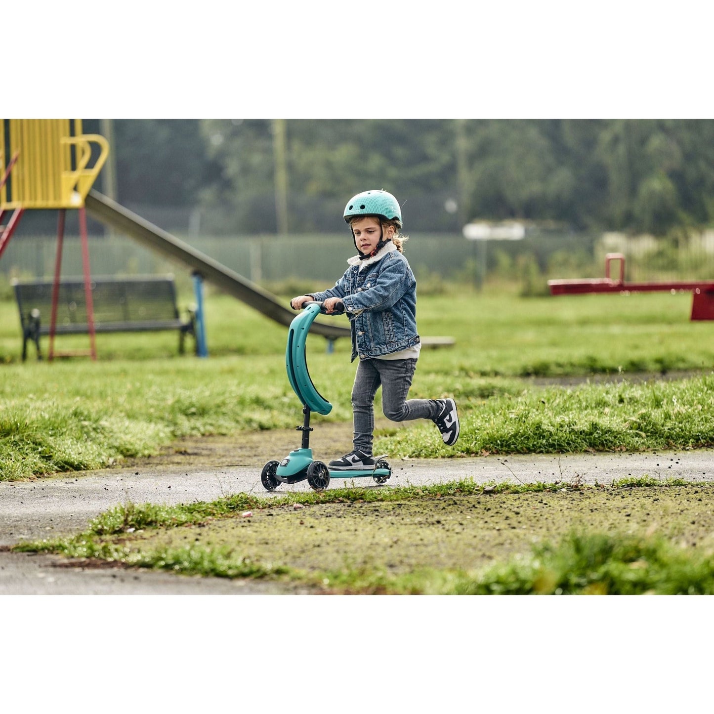 boy riding ride-ezy scooter in the park and wearing Ride-Ezy Hector 48-53cms Kids Helmet - Woodland Green