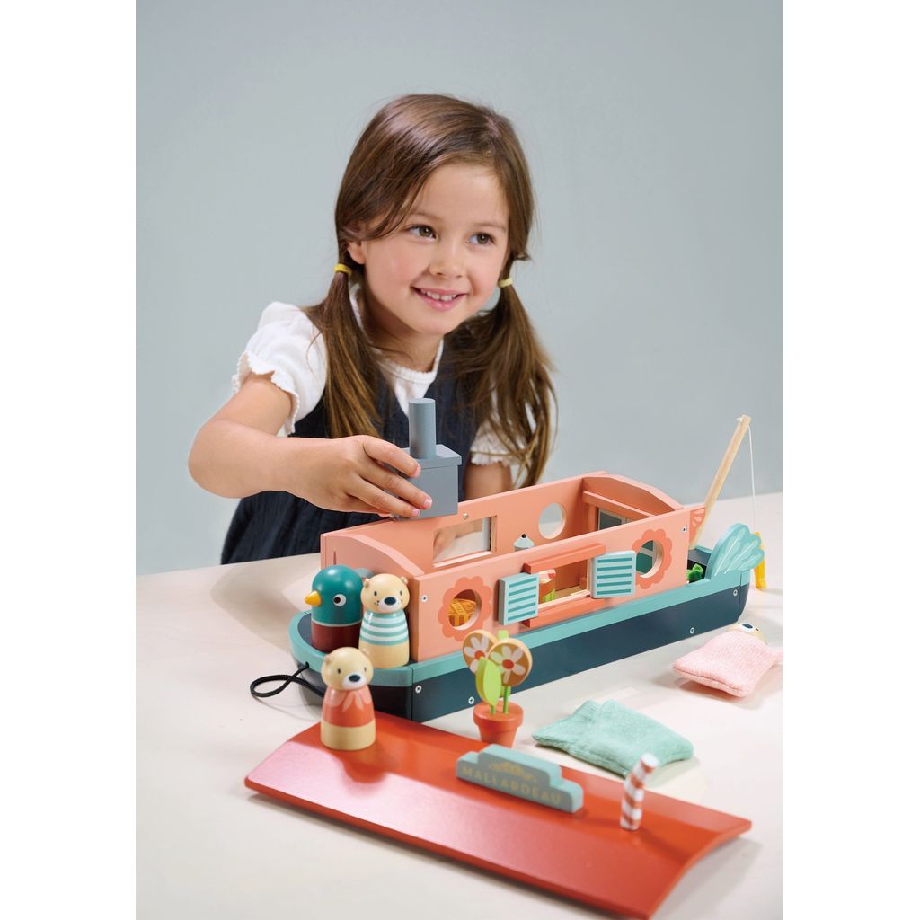 smiling girl sitting at table with Tender Leaf Little Otter Canal Boat Wooden Toy
