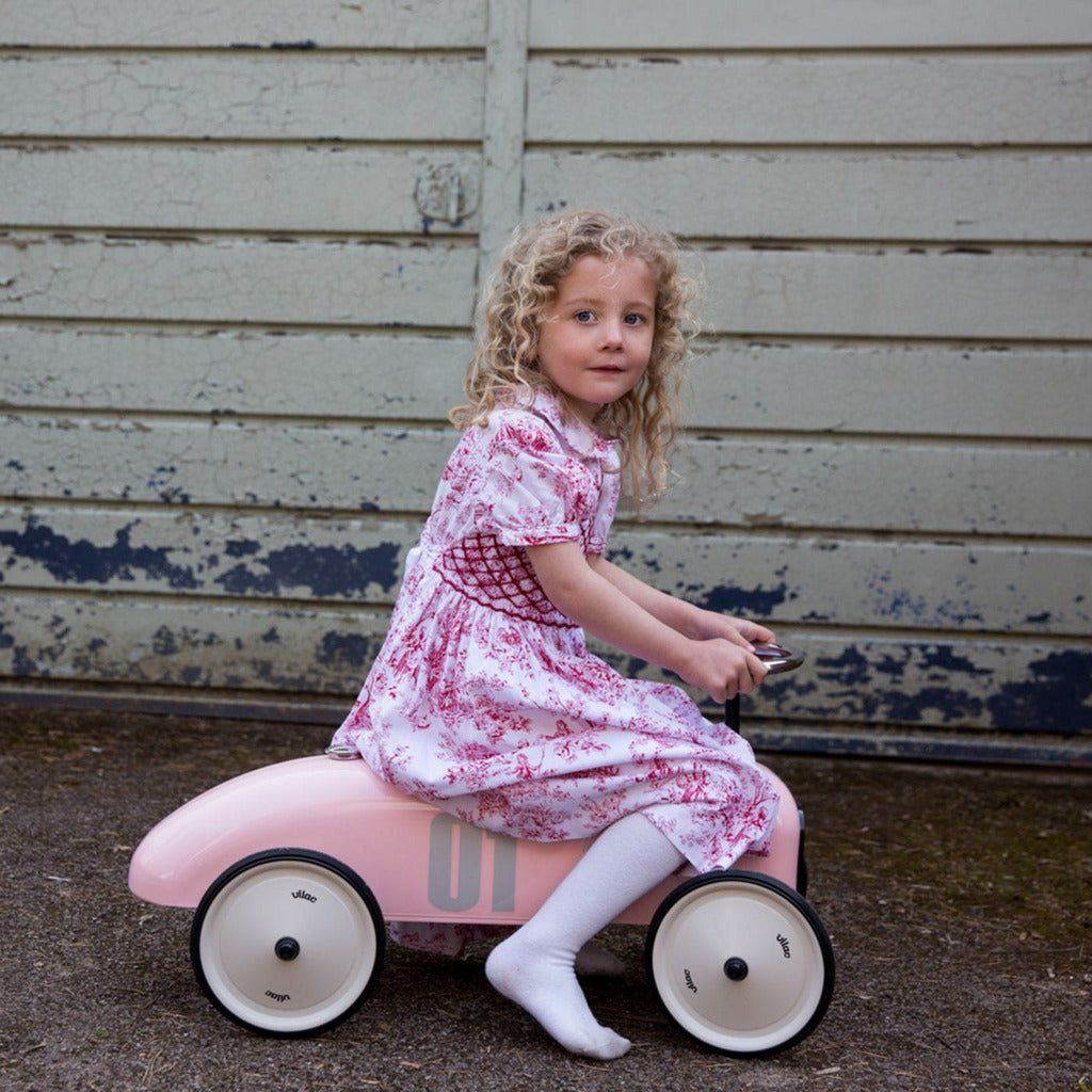 little girl in dress riding Vilac Classic Ride-On Racing Car - 18m+ - Pink