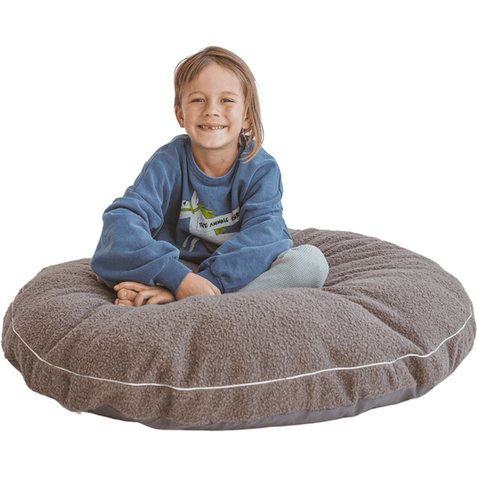 smiling child sitting on MINICAMP Boucle Fabric Kids Floor Cushion in Grey