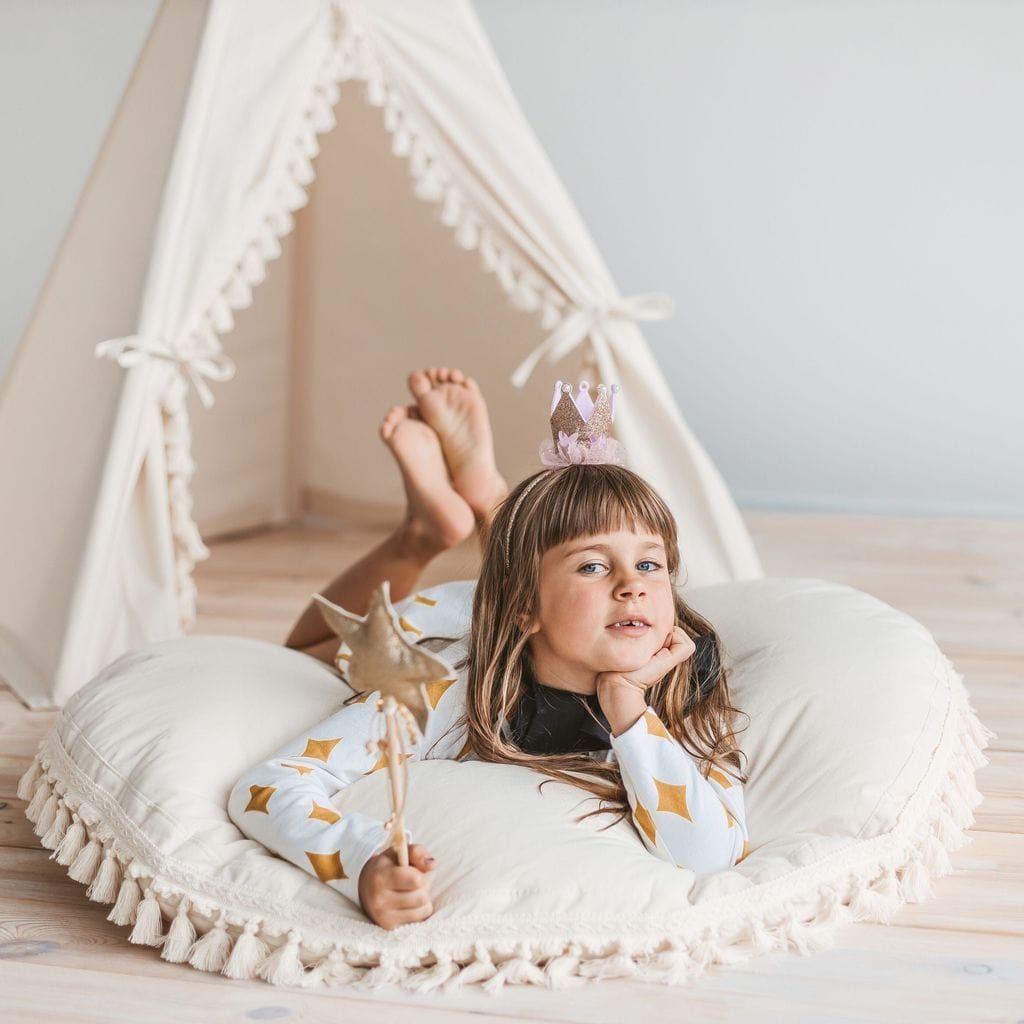 girl lying on floor cushion in front of MINICAMP Boho Kids Teepee With Tassels