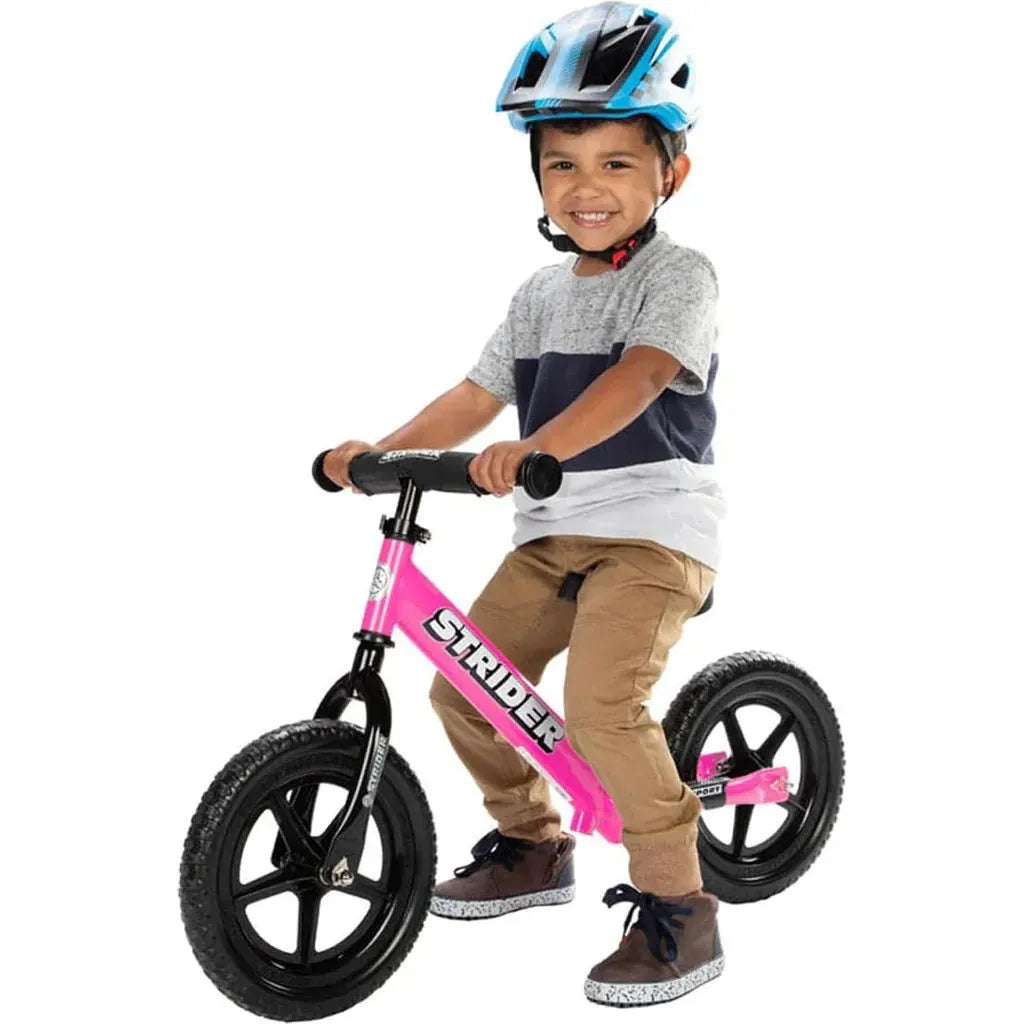 smiling boy sitting on Strider Sport 12 inch Balance Bike - Pink