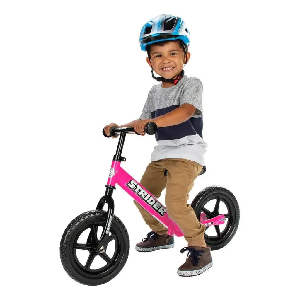 smiling boy riding Strider Classic 12 inch Balance Bike - Pink