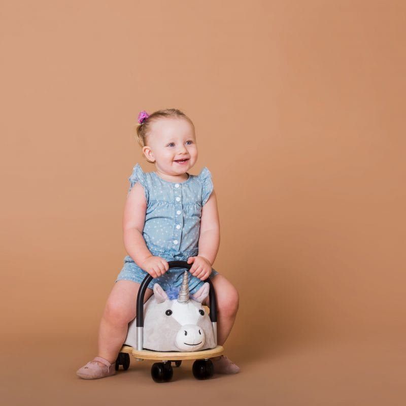 little girl sitting on Wheelybug Plush Ride On - Unicorn